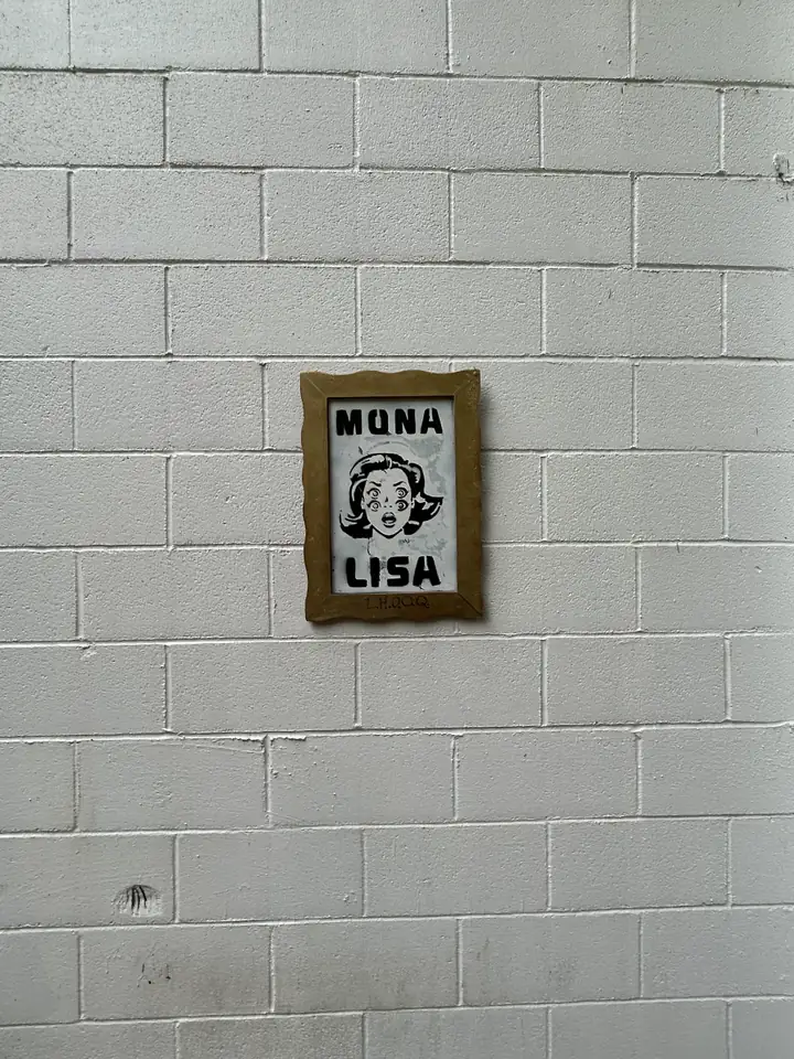 The first Mona Lisa hanging in its gold frame on a white cinder-block wall