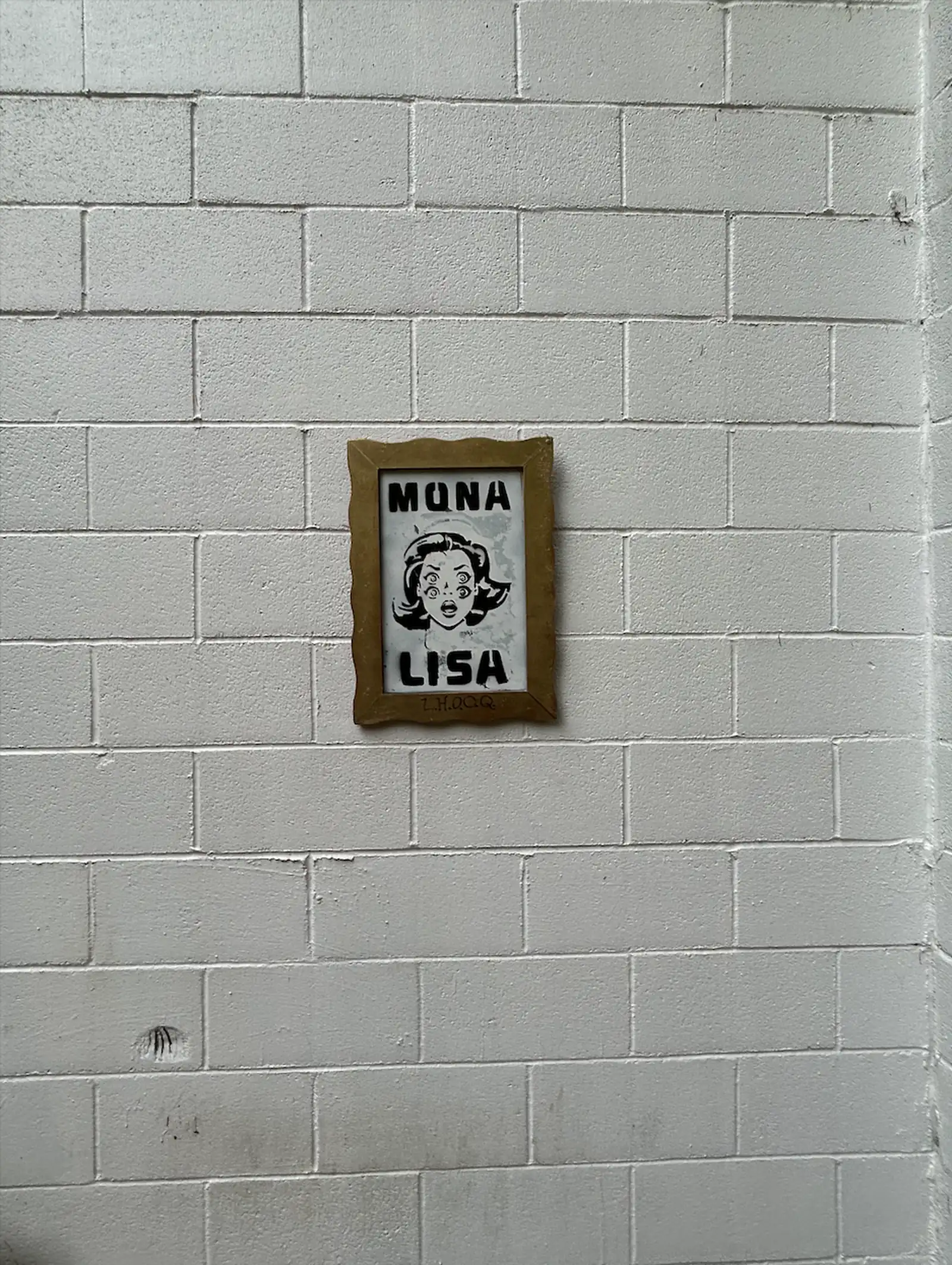 norville’s framed Mona Lisa hanging on a white cinder-block wall