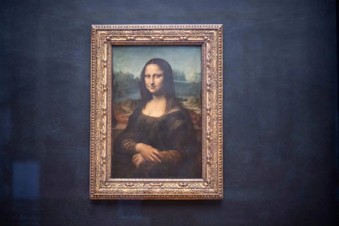 The Mona Lisa in its gilt frame on a dark wall at the Louvre