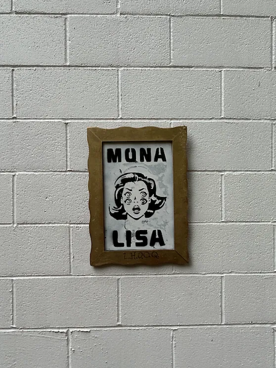 The same framed Mona Lisa hanging alone on a white cinder-block wall